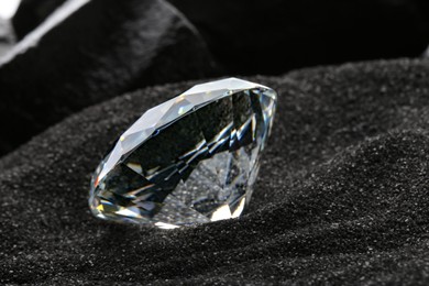 Photo of Beautiful shiny diamond on decorative black sand, closeup