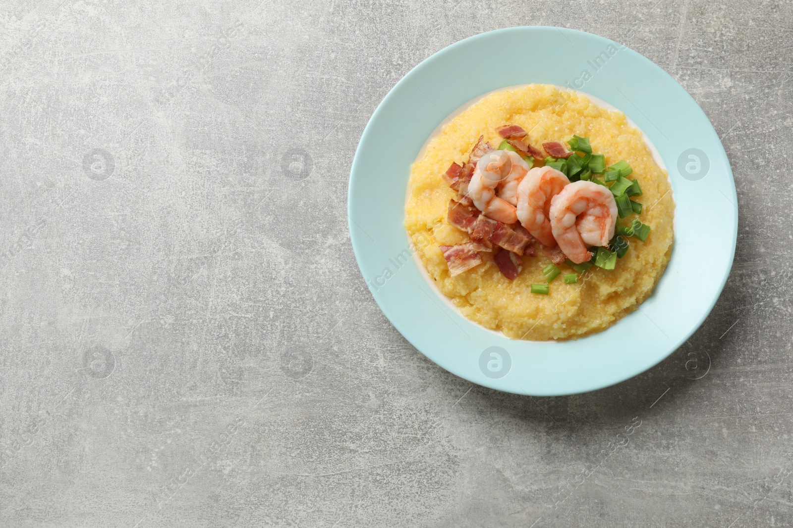 Photo of Plate with fresh tasty shrimps, bacon, grits and green onion on grey table, top view. Space for text