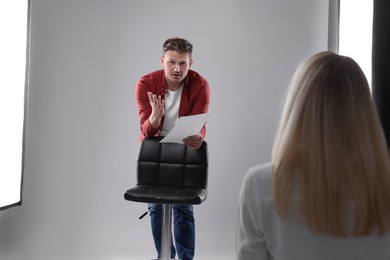 Photo of Man with script performing in front of casting director against light grey background in studio