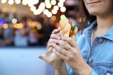 Photo of Young woman holding delicious bubble waffle with tomato and arugula outdoors, closeup