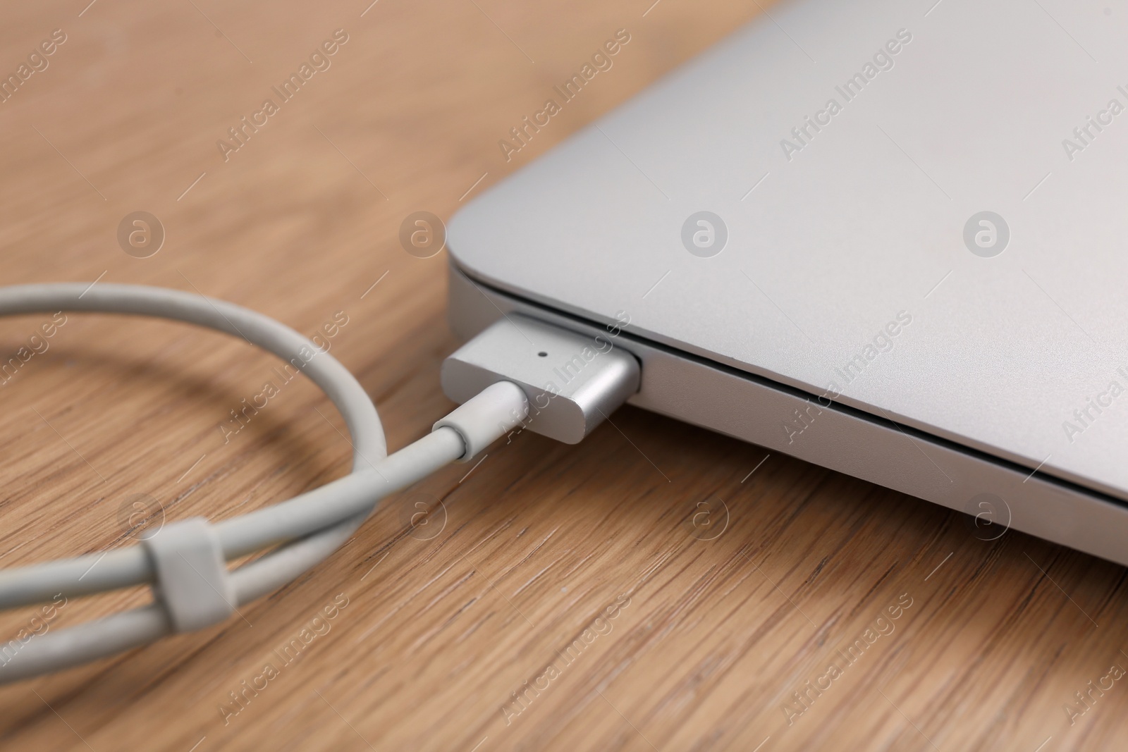 Photo of Modern laptop and charging cable on wooden table, closeup