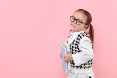 Photo of Cute little girl in glasses with books on pink background. Space for text