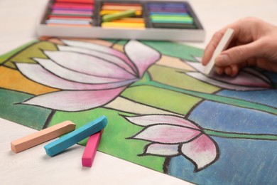 Photo of Woman drawing beautiful lotus flowers on paper with soft pastels at white table, closeup