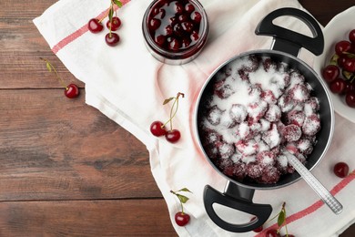 Photo of Flat lay composition of pot with cherries and sugar on wooden table, space for text. Making delicious jam