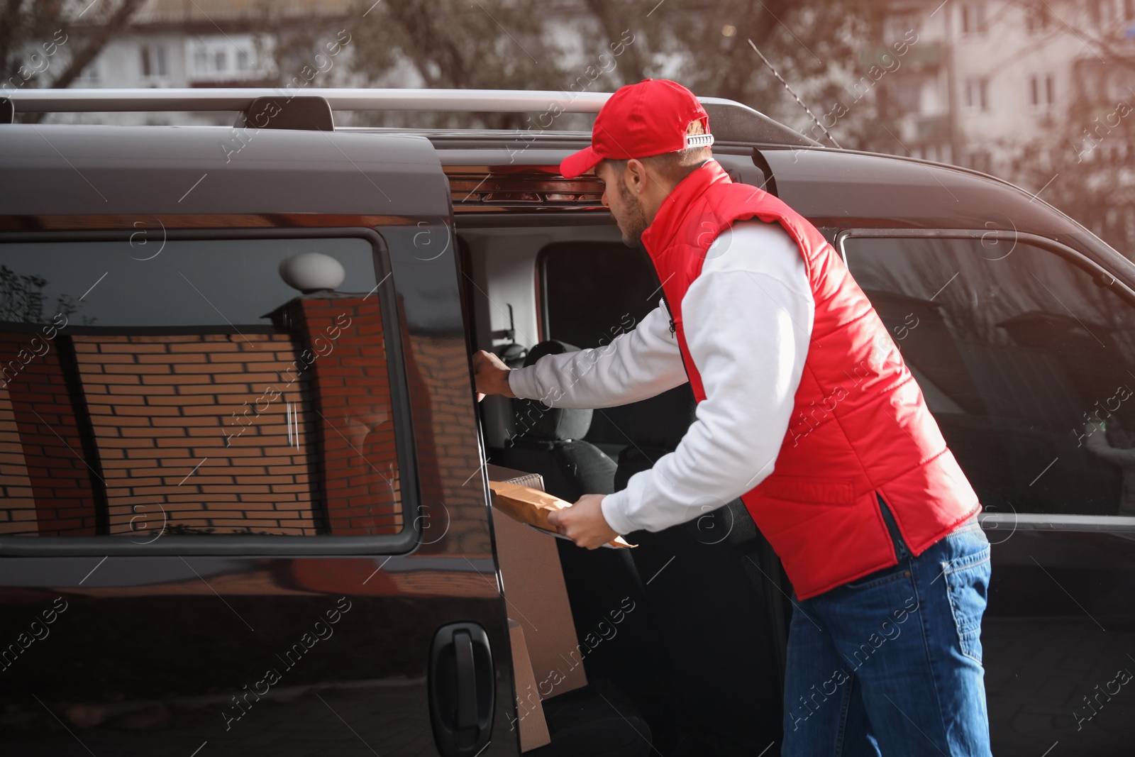 Photo of Deliveryman in uniform taking parcel from van outdoors