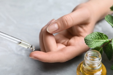 Woman dripping essential oil onto her finger at table, closeup