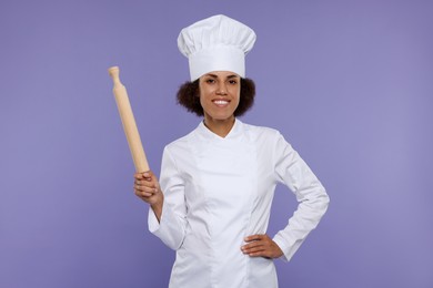 Photo of Happy female chef in uniform holding rolling pin on purple background