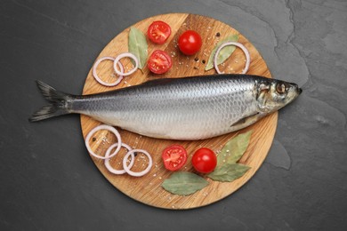 Tray with salted herring, onion rings, bay leaves and cherry tomatoes on black table, top view