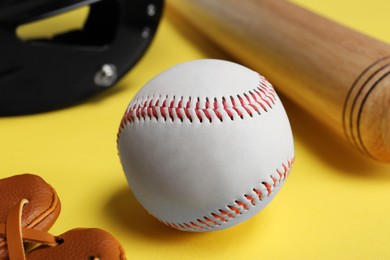 Baseball ball and bat on yellow background, closeup
