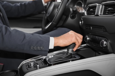 Photo of Man holding hand on gear lever in modern car, closeup