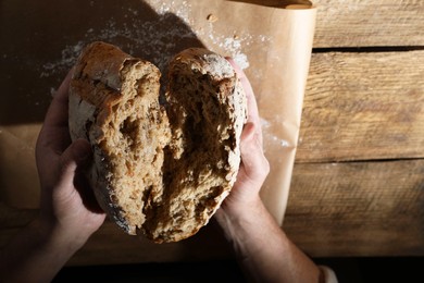 Photo of Man breaking loaf of fresh bread at wooden table, top view. Space for text