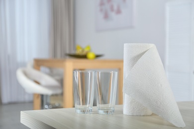 Roll of paper towels and glasses on table indoors. Space for text