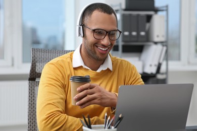 Young man with cup of drink working on laptop in office