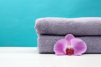 Photo of Soft clean towels with beautiful flower on table against color background. Space for text