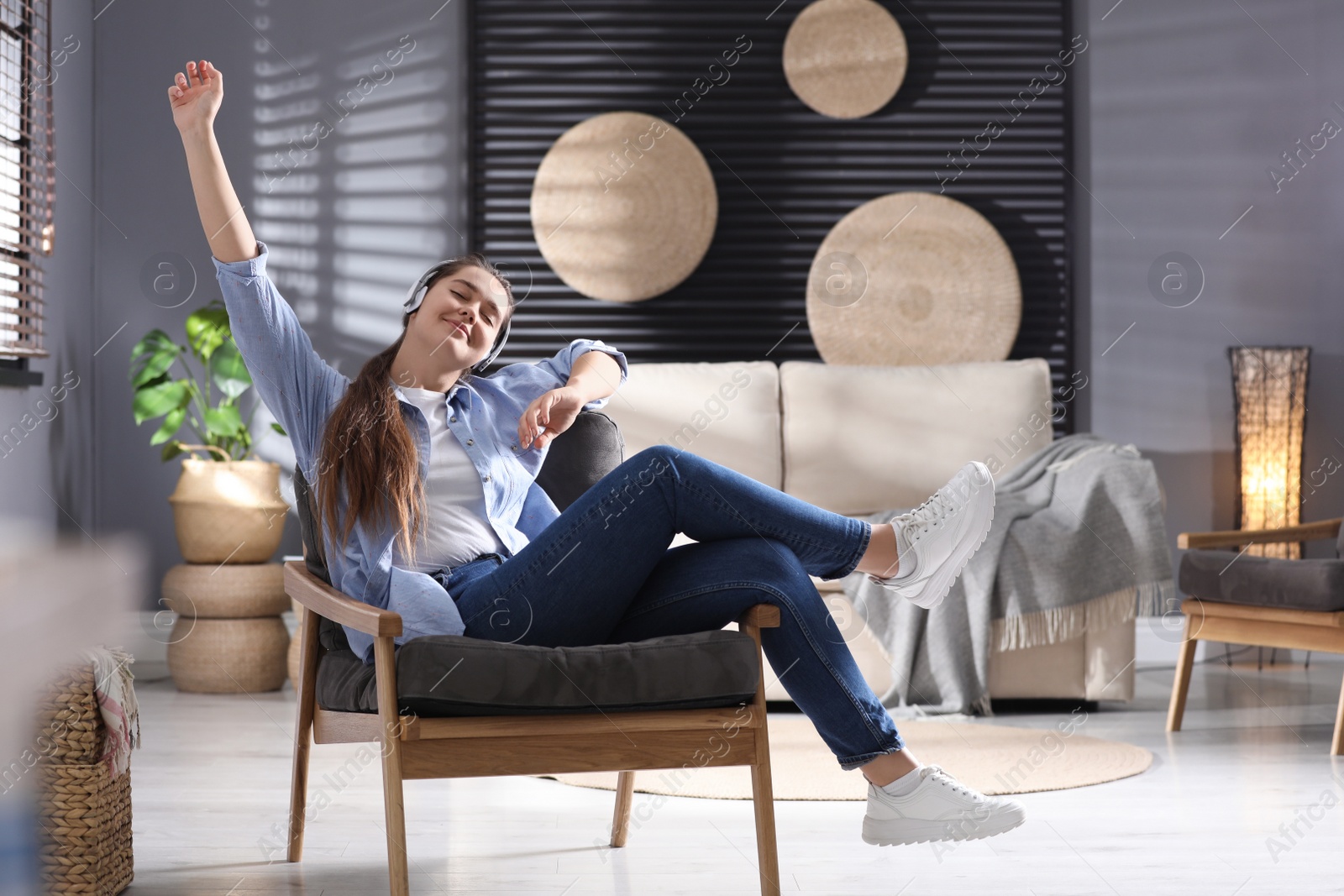 Photo of Young woman with headphones listening to music in armchair at home