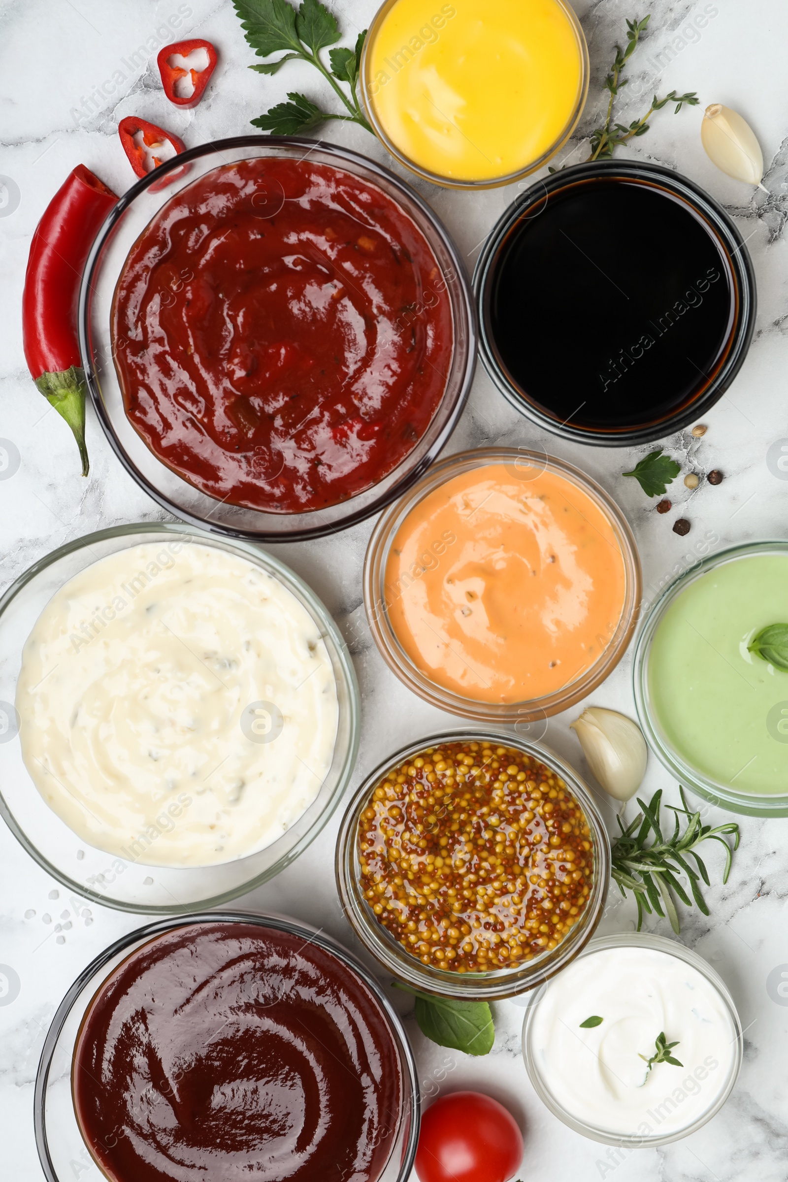 Photo of Many different sauces and herbs on white marble table