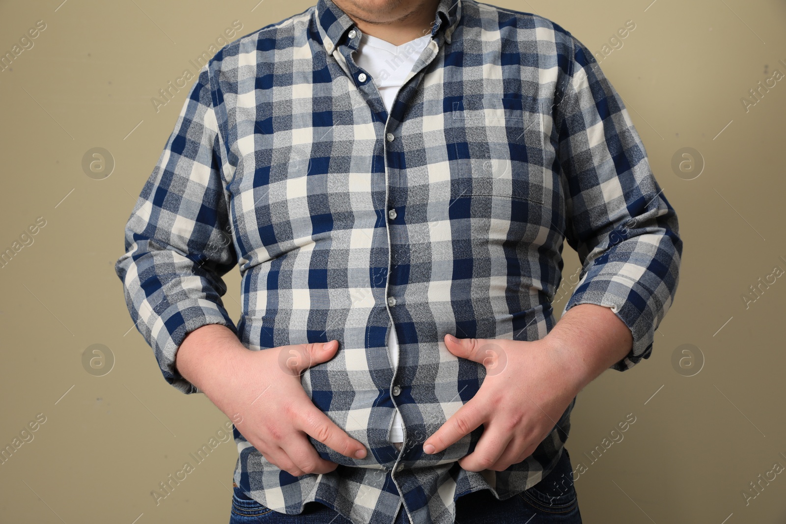Photo of Overweight man in tight shirt on beige background, closeup