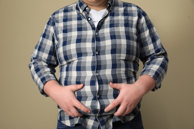 Photo of Overweight man in tight shirt on beige background, closeup