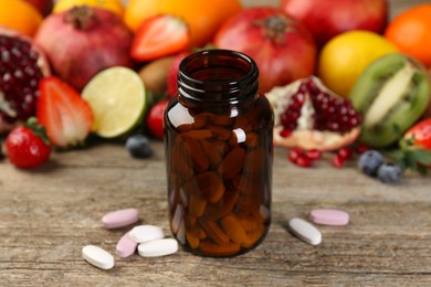 Photo of Vitamin pills, bottle and fresh fruits on wooden table