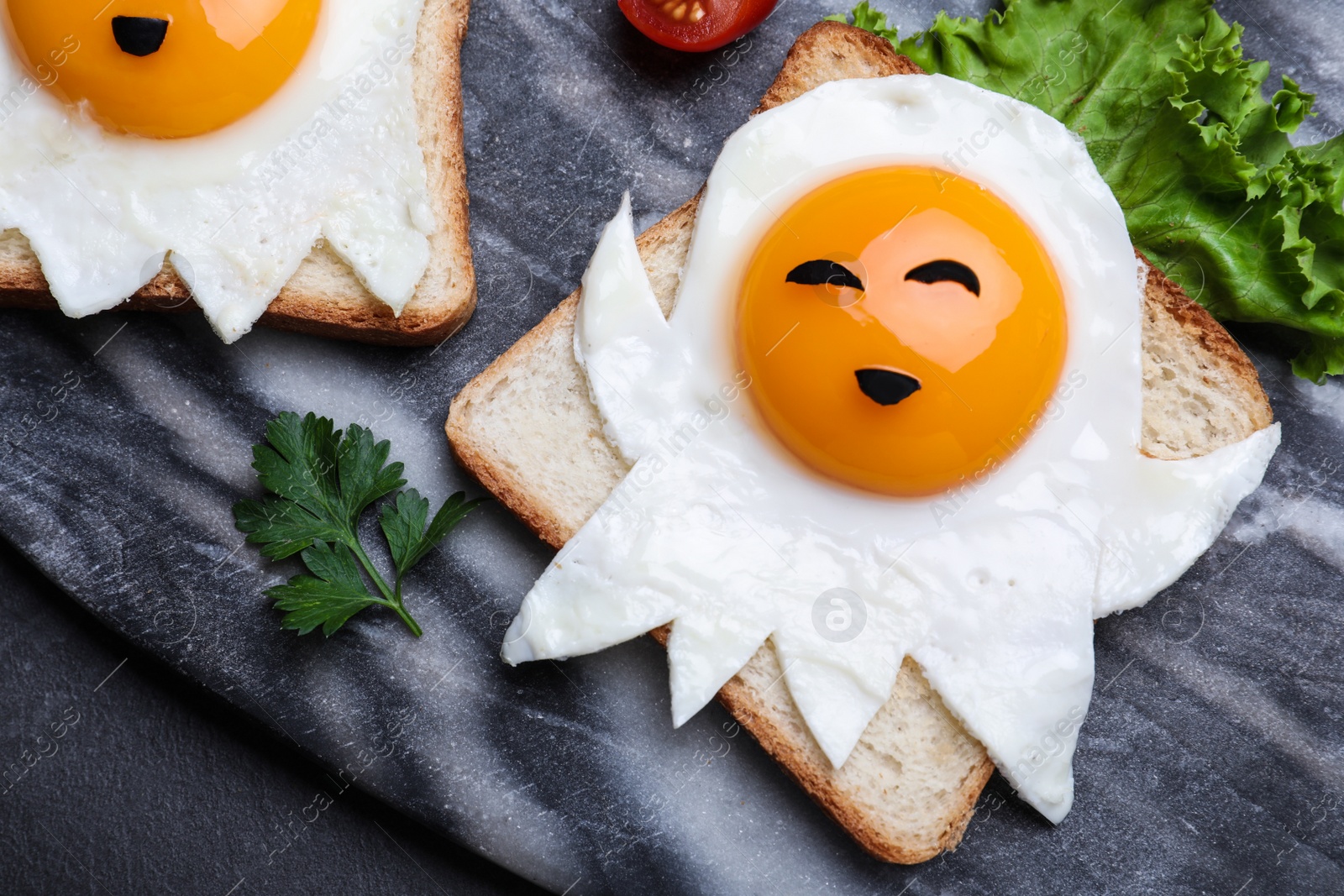 Photo of Halloween themed breakfast served on black table, flat lay. Tasty toasts with fried eggs in shape of ghost