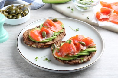 Photo of Delicious sandwiches with salmon, avocado and capers on white wooden table