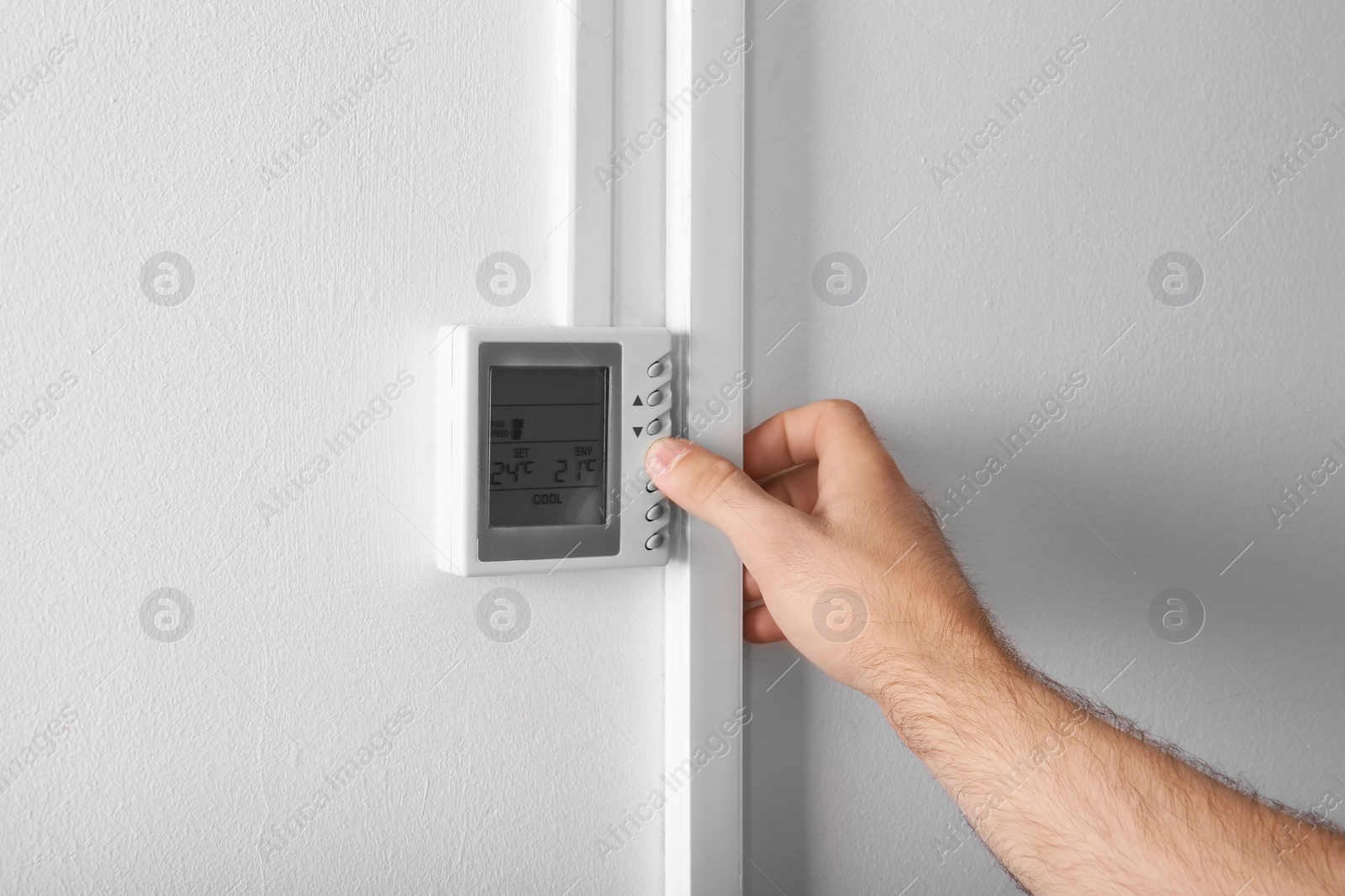 Photo of Man adjusting thermostat on white wall, closeup. Heating system