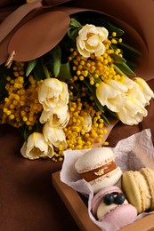 Photo of Bouquet of beautiful spring flowers and macarons on brown fabric
