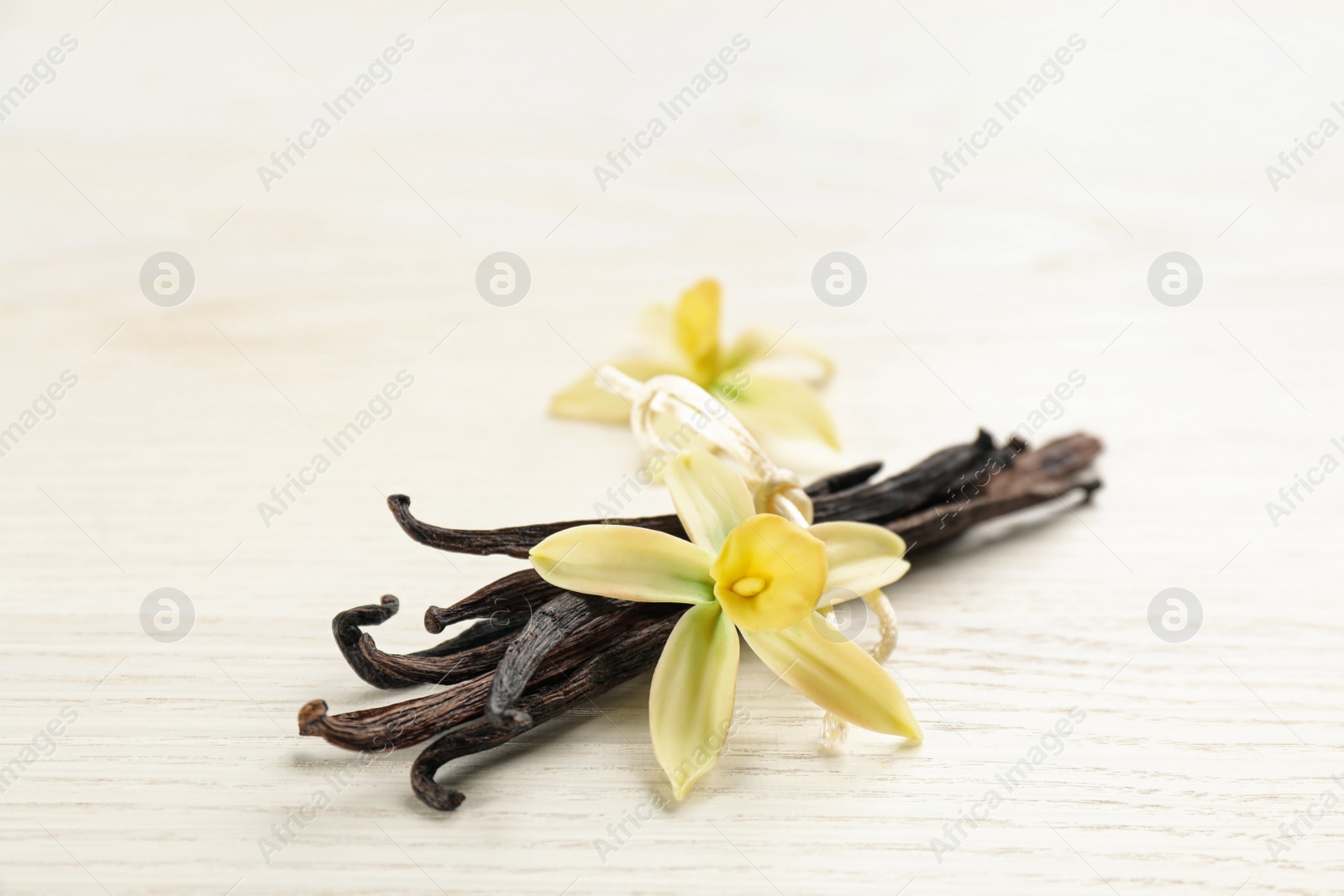 Photo of Beautiful vanilla flowers and sticks on white wooden table, closeup