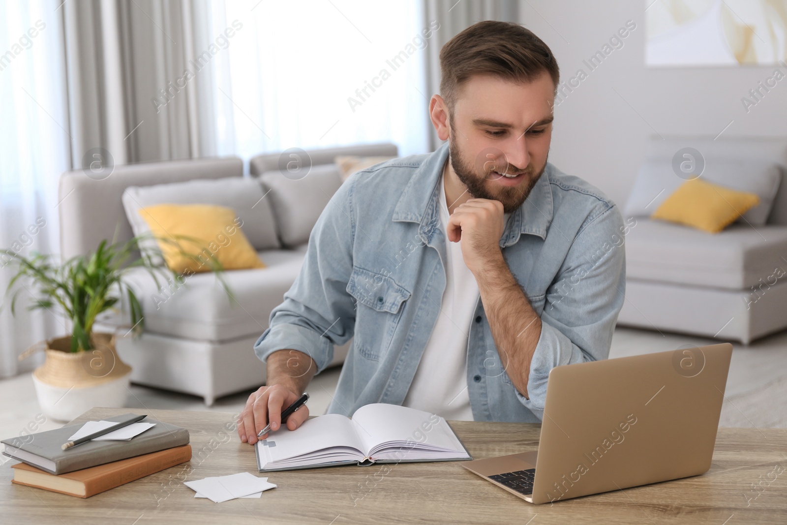 Photo of Young man watching online webinar at table indoors