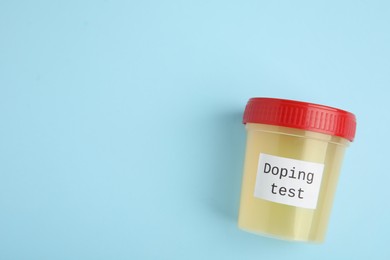 Photo of Top view of jar with urine sample on light blue background, space for text. Doping control