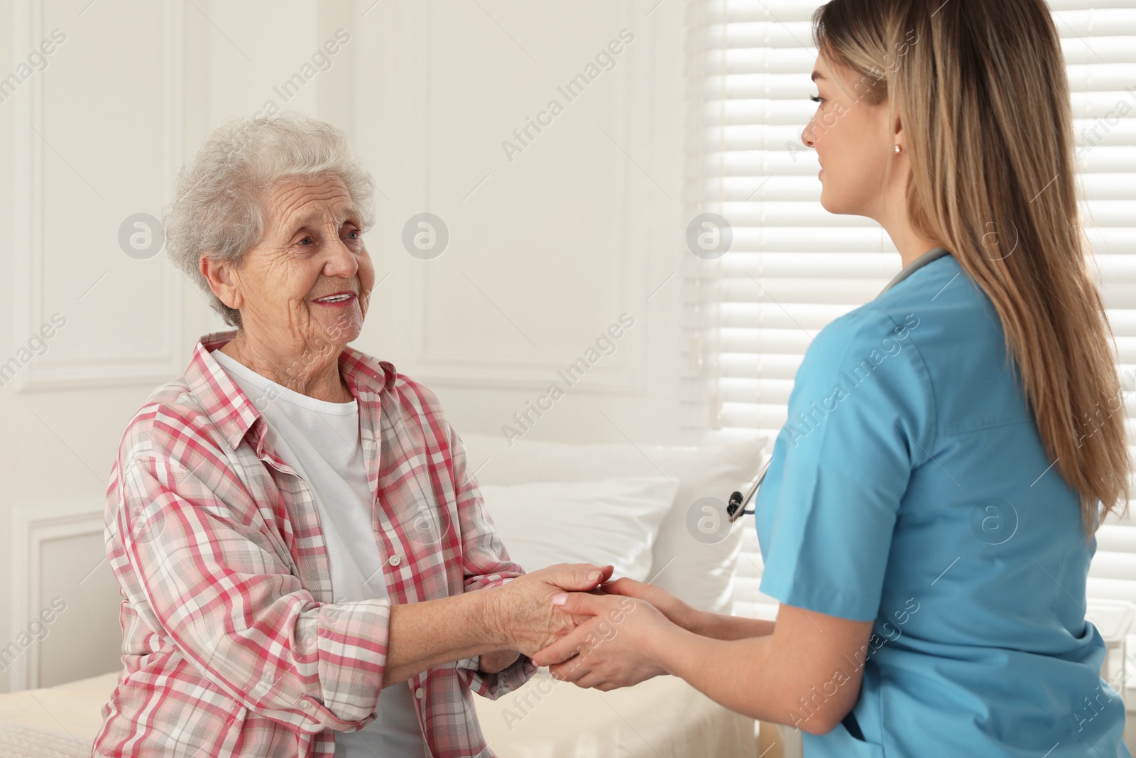 Photo of Young caregiver talking to senior woman in room. Home health care service