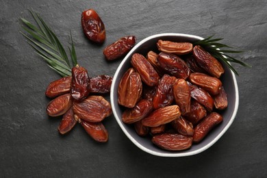 Photo of Tasty sweet dried dates and green leaves on black table, flat lay