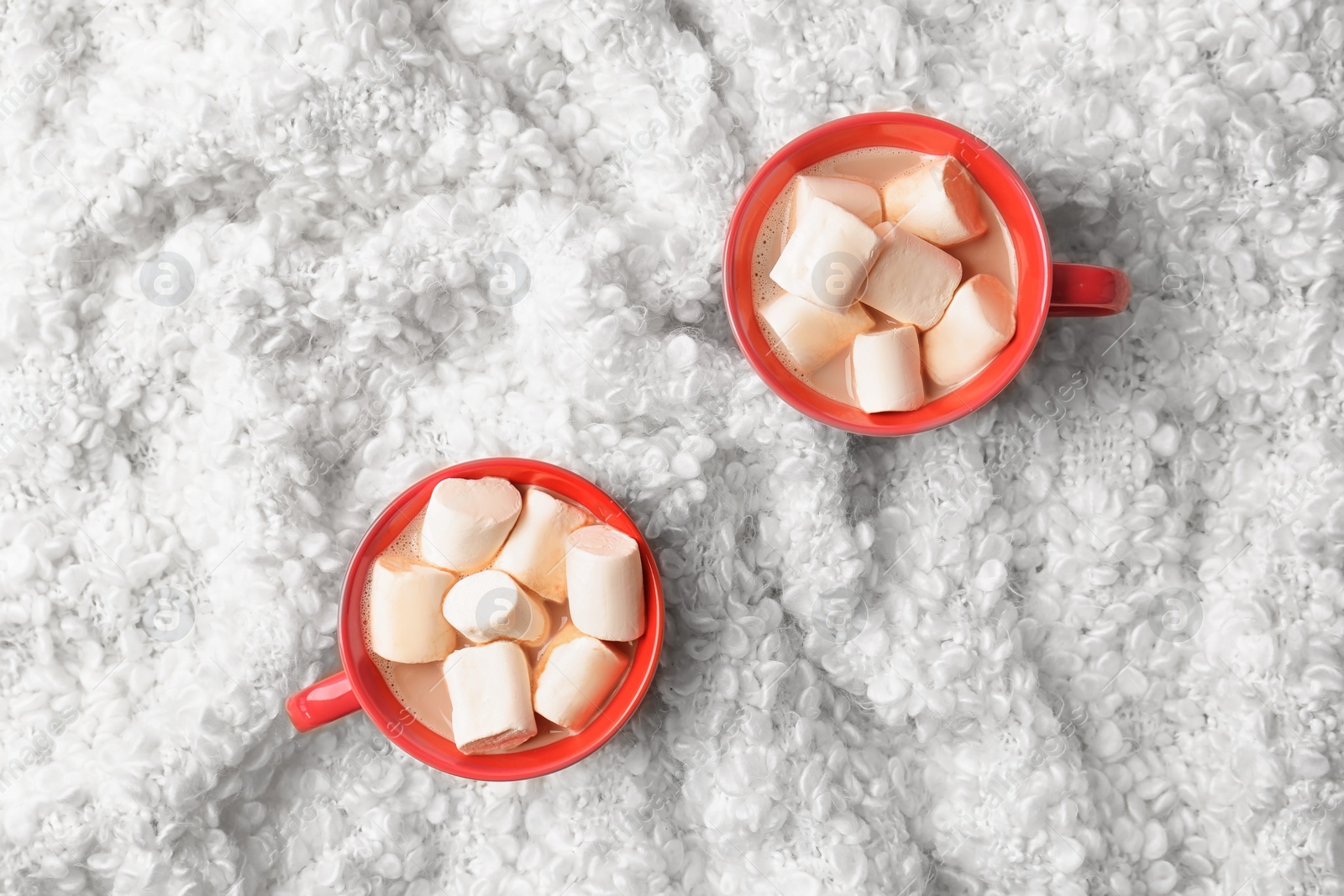 Photo of Hot cocoa drink with marshmallows in cups on fabric, top view