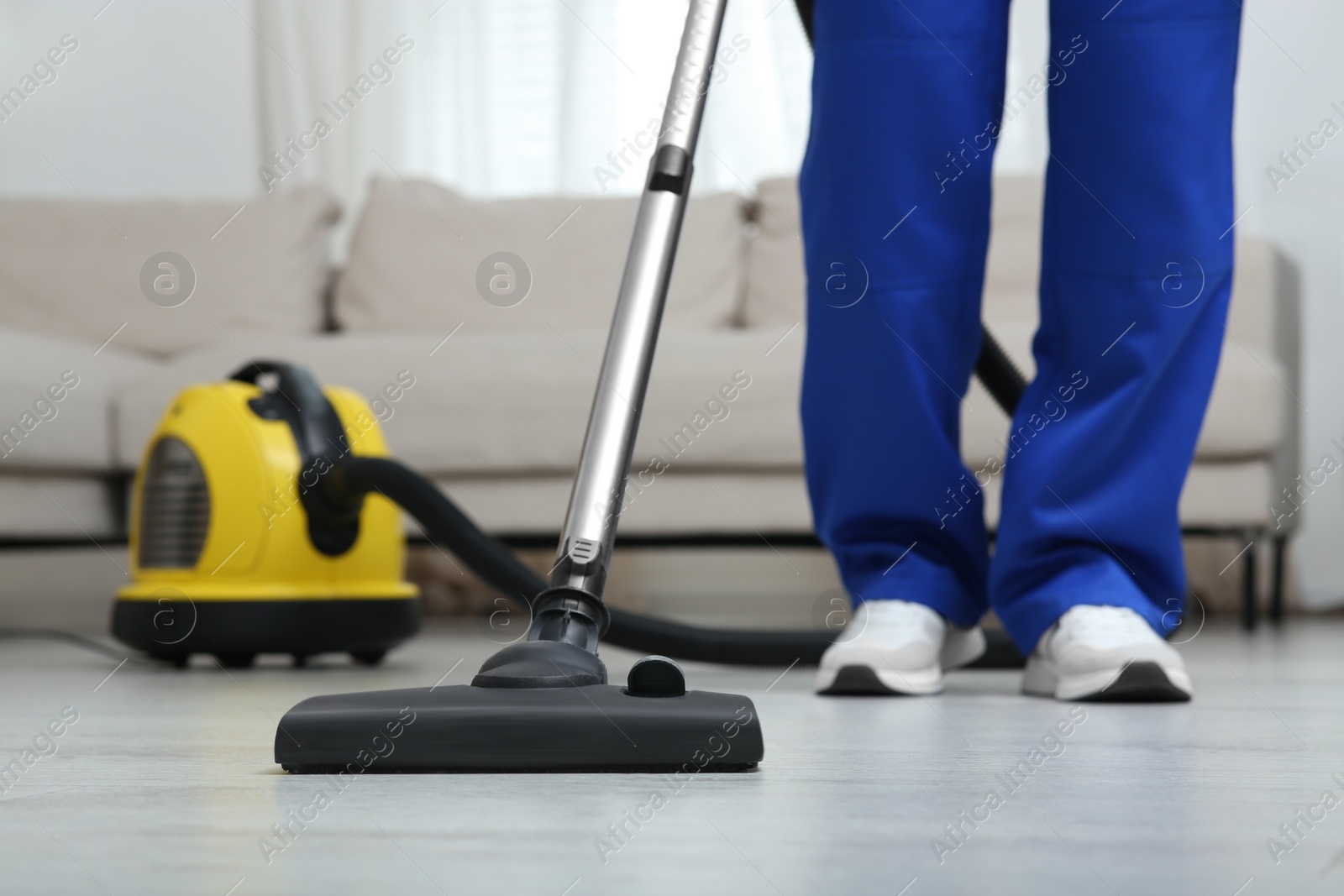 Photo of Janitor in uniform vacuuming floor indoors, closeup