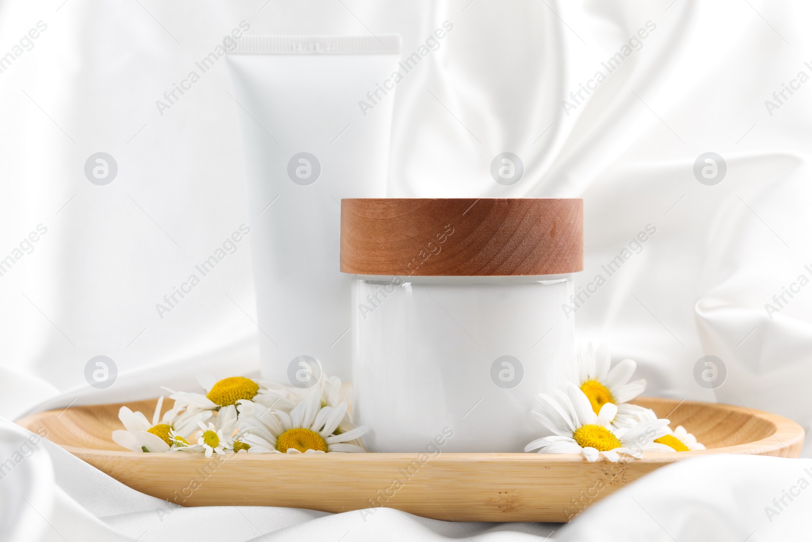 Photo of Different hand care cosmetic products and chamomiles on white silk fabric