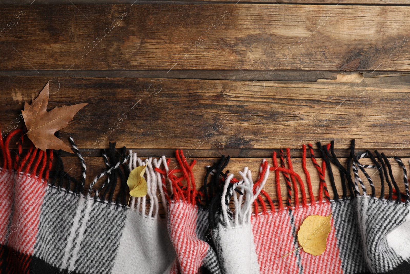 Photo of Checkered plaid and dry leaves on wooden table, flat lay. Space for text