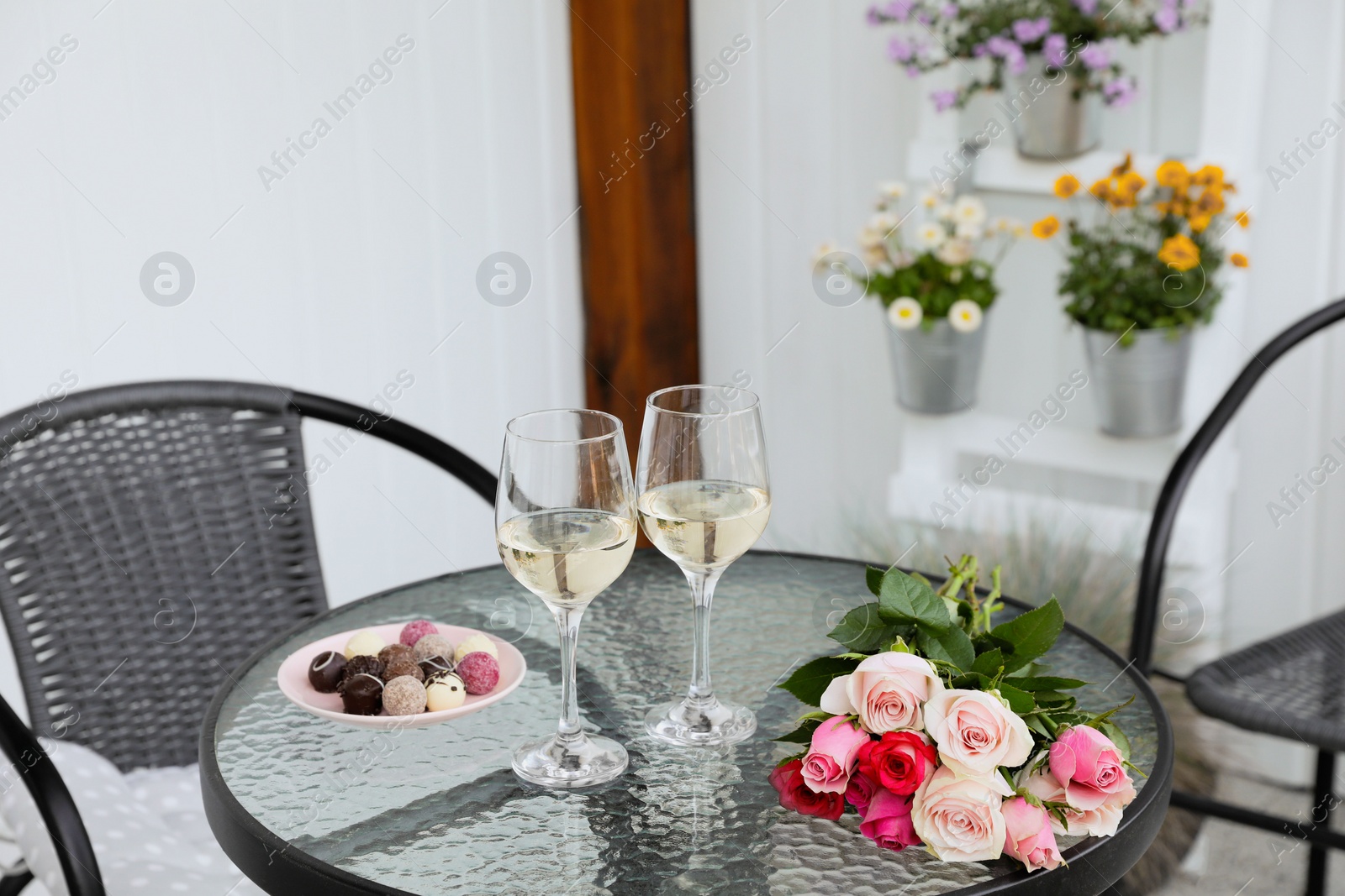 Photo of Bouquet of roses, glasses with wine and candies on glass table on outdoor terrace