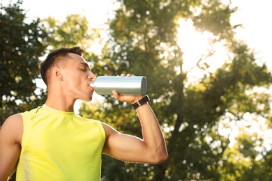Sporty man drinking from water bottle at park on sunny day. Space for text