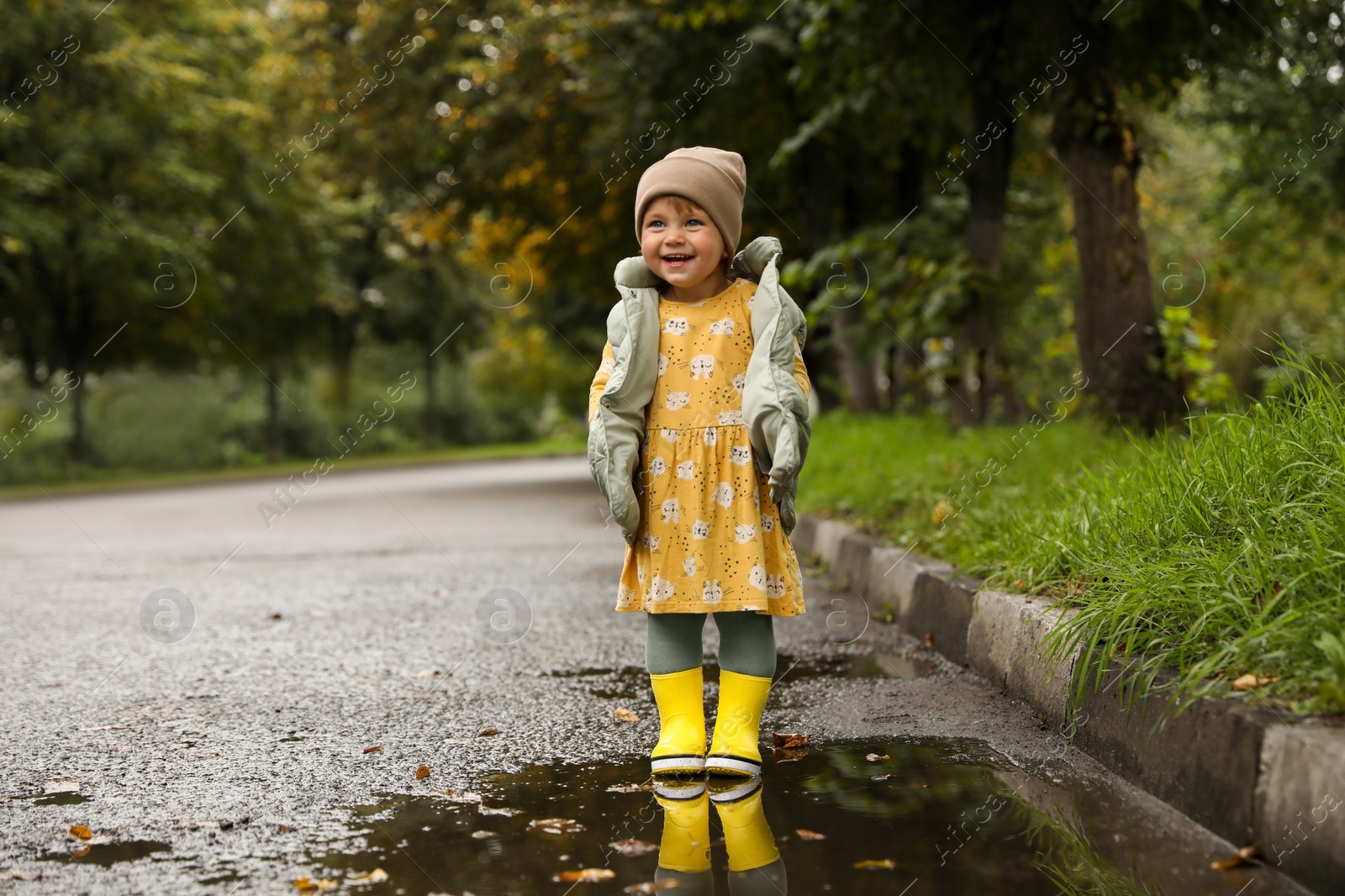 Photo of Cute little girl standing in puddle outdoors