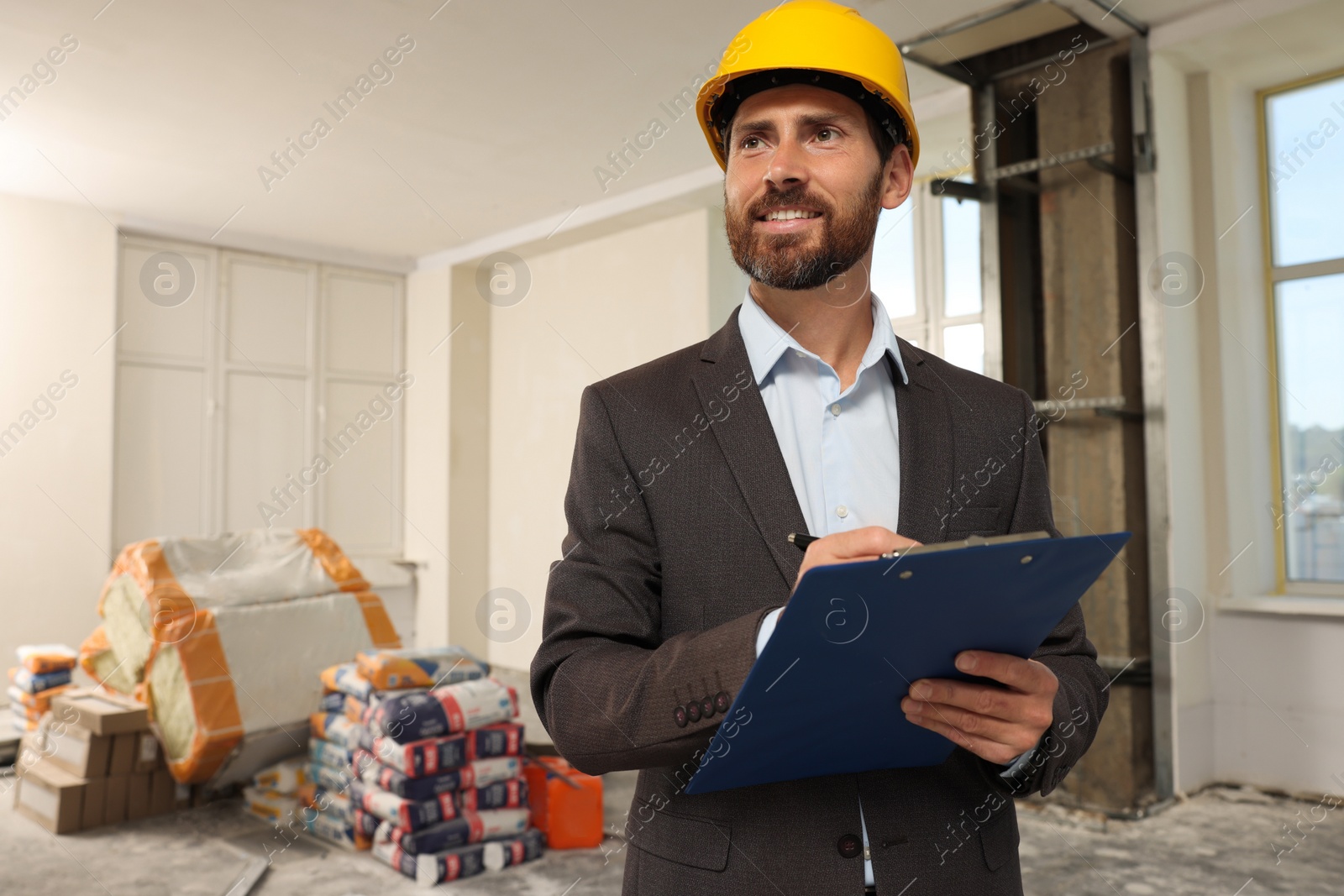 Photo of Professional engineer in hard hat with clipboard indoors