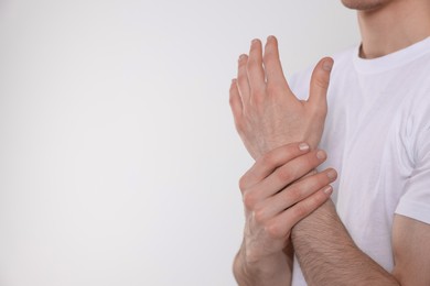 Man suffering from pain in his hand on light background, closeup view with space for text. Arthritis symptoms
