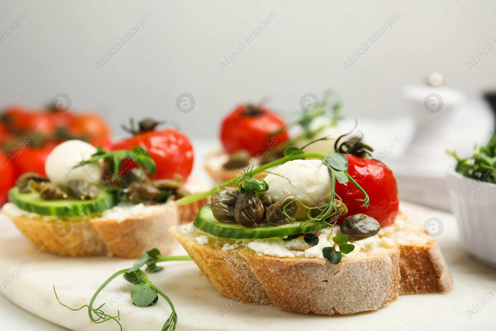 Photo of Tasty bruschettas with capers, vegetables and mozzarella served on white marble board, closeup