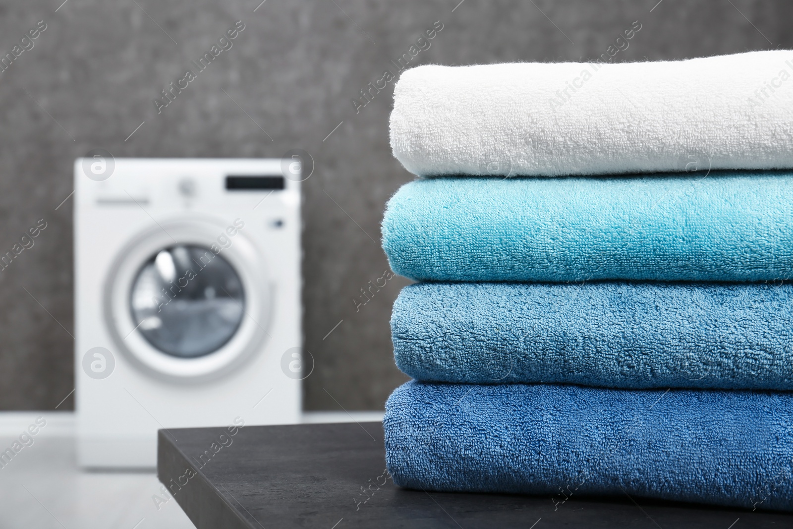 Photo of Stack of clean towels on table in laundry room, closeup. Space for text