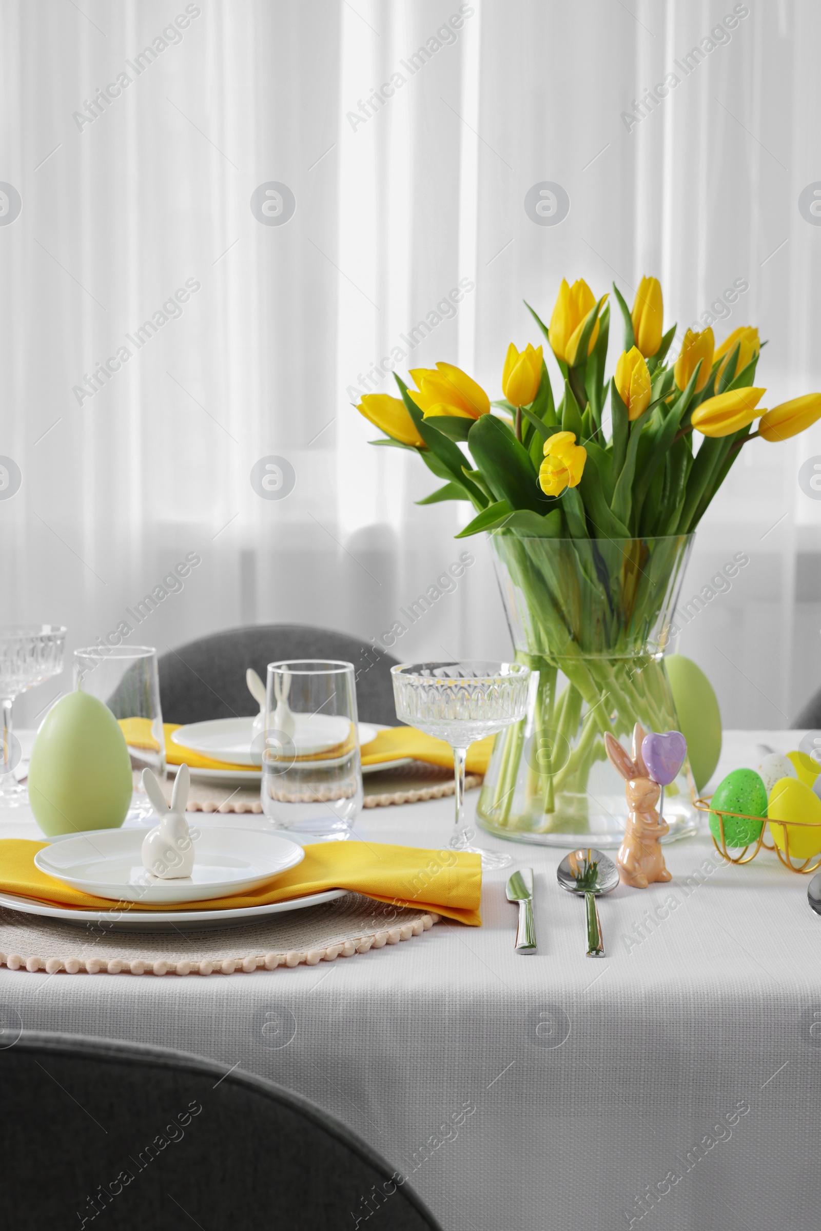 Photo of Festive table setting with glasses, painted eggs and vase of tulips. Easter celebration