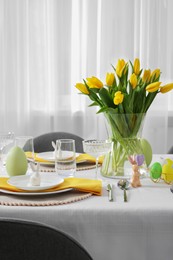 Festive table setting with glasses, painted eggs and vase of tulips. Easter celebration