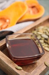 Photo of Glass bowl of oil and pumpkin seeds on wooden tray, closeup