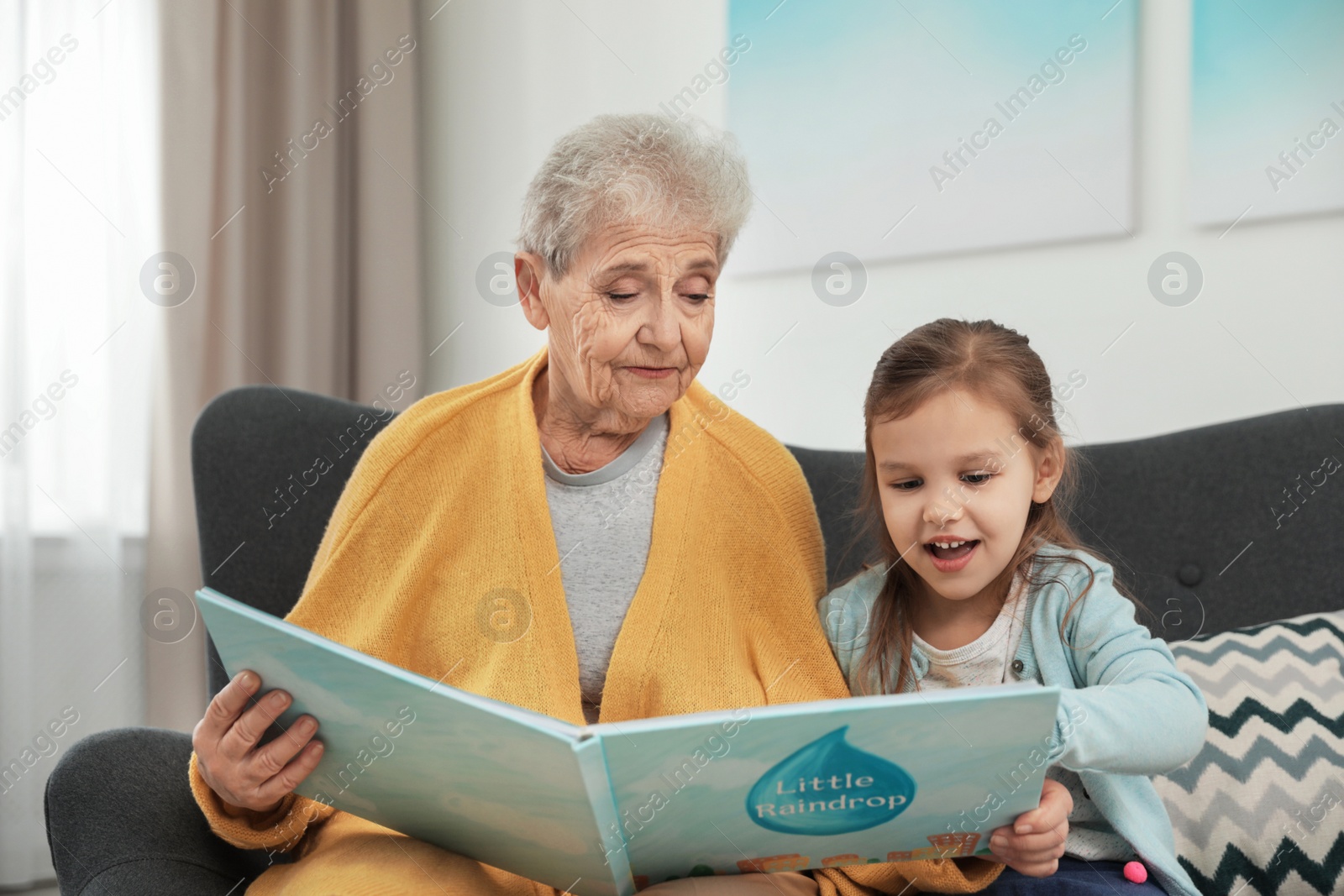 Photo of Cute girl and her grandmother reading book at home