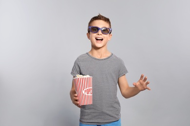 Boy with 3D glasses and popcorn during cinema show on grey background