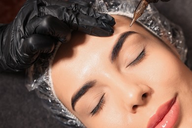 Photo of Young woman undergoing procedure of permanent eyebrow makeup in tattoo salon, top view