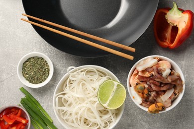 Flat lay composition with black wok, spices and products on grey textured table